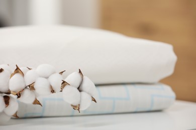 Bed sheets and cotton branch with fluffy flowers on white table indoors, closeup