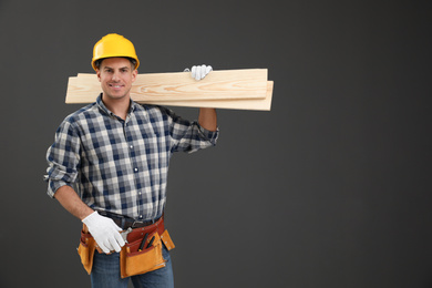 Photo of Handsome carpenter with wooden planks on dark background. Space for text