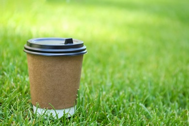 Photo of Disposable paper cup with plastic lid on fresh green grass outdoors