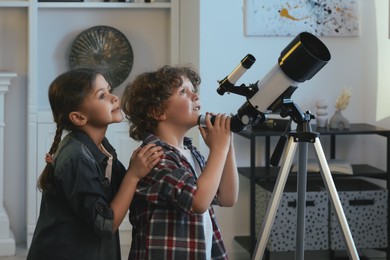 Photo of Cute little children using telescope to look at stars in room