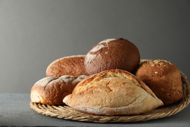 Photo of Wicker basket with different types of fresh bread on grey wooden table, closeup