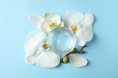 Flat lay composition with cosmetic gel and beautiful flowers on light blue background