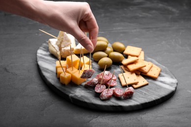 Woman taking toothpick with piece of sausage at black table, closeup