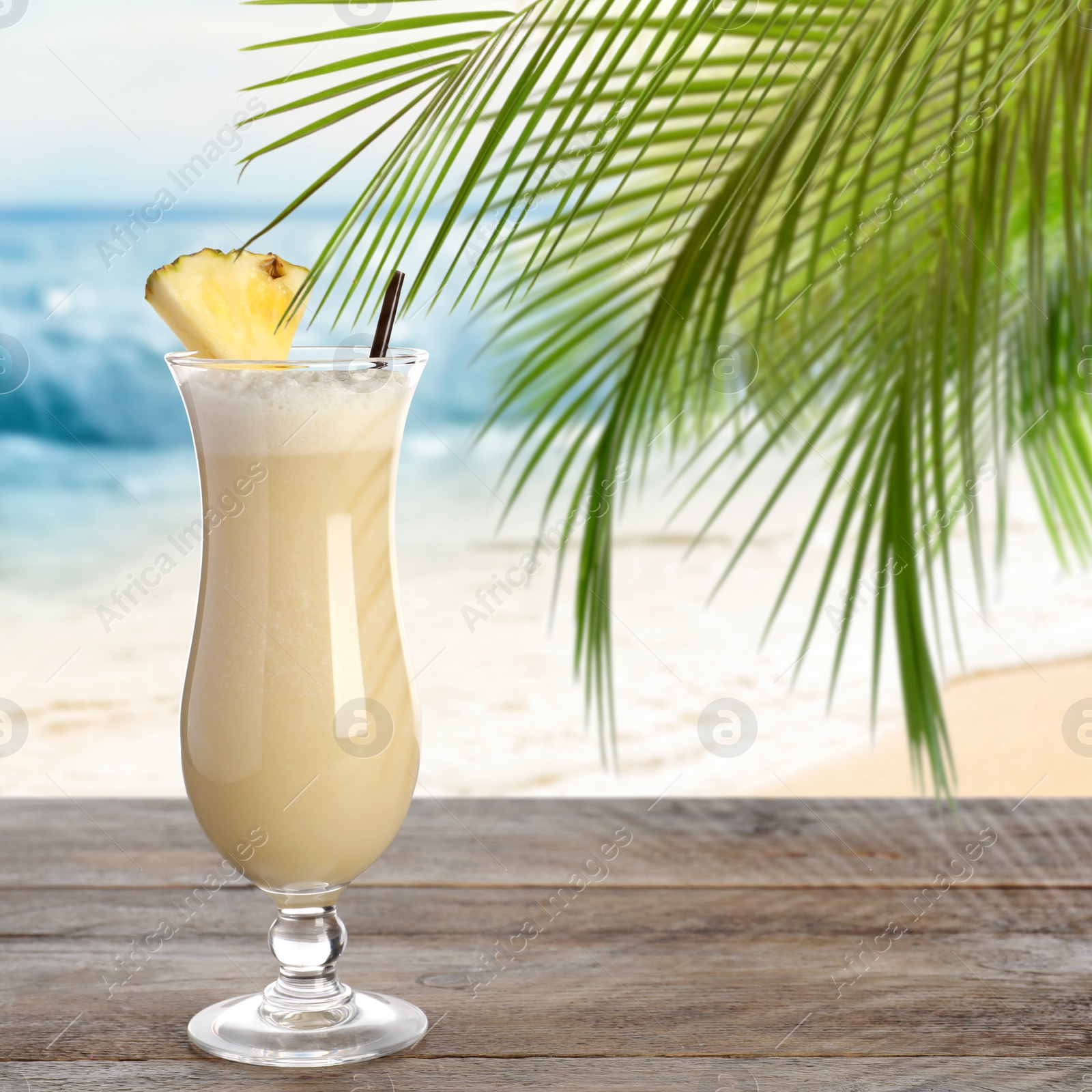 Image of Tasty Pina Colada cocktail on wooden table near ocean. Space for text