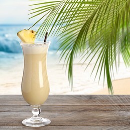 Image of Tasty Pina Colada cocktail on wooden table near ocean. Space for text