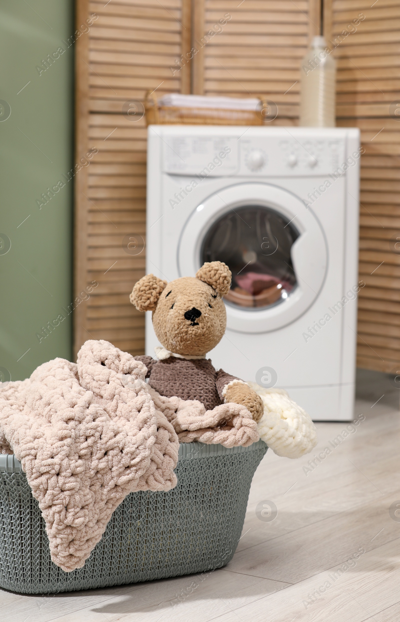 Photo of Laundry basket with soft blankets and toy in bathroom