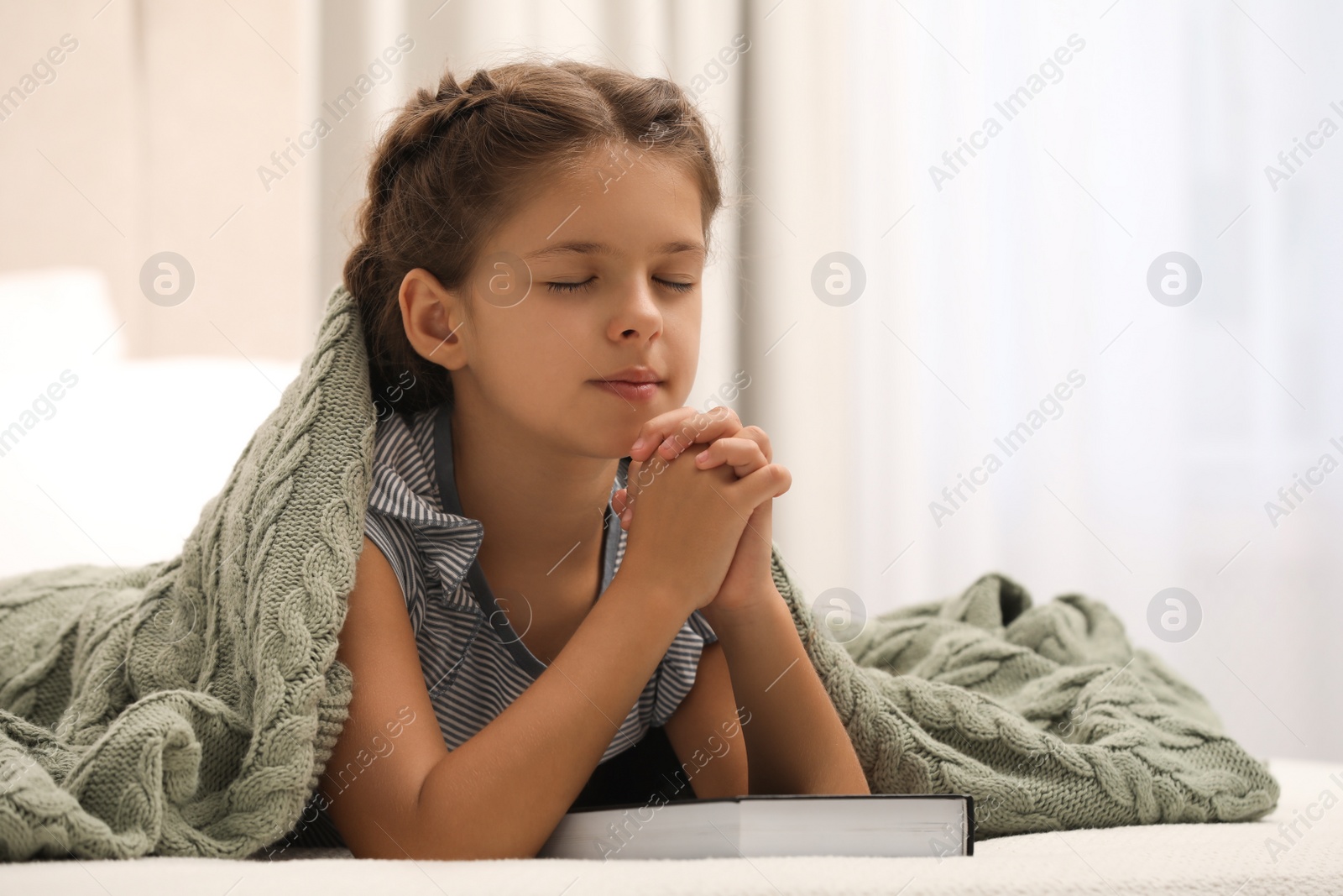 Photo of Cute little girl praying over Bible in bedroom