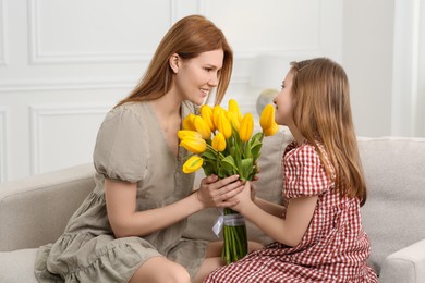 Daughter congratulating mom with bouquet of yellow tulips at home