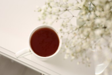 Photo of Ceramic mug with tea on white bedside table indoors, top view