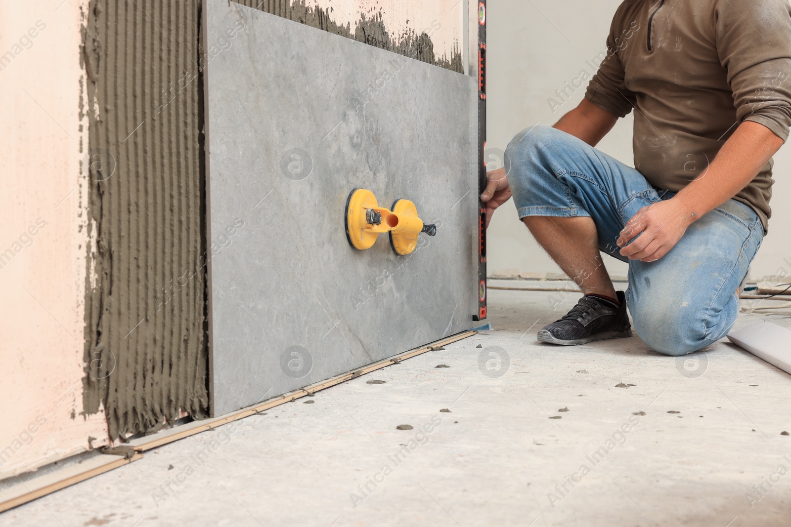 Photo of Professional worker installing tile on wall indoors, closeup