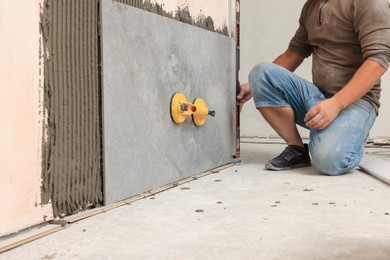 Photo of Professional worker installing tile on wall indoors, closeup