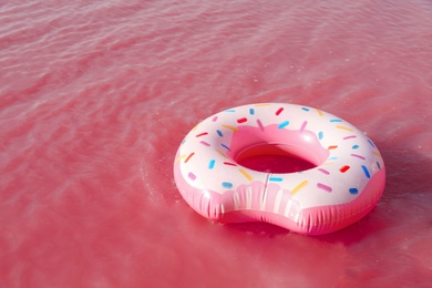 Photo of Bright inflatable ring floating in pink lake on summer day