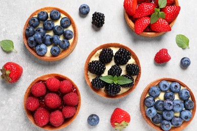 Tartlets with different fresh berries on light grey table, flat lay. Delicious dessert