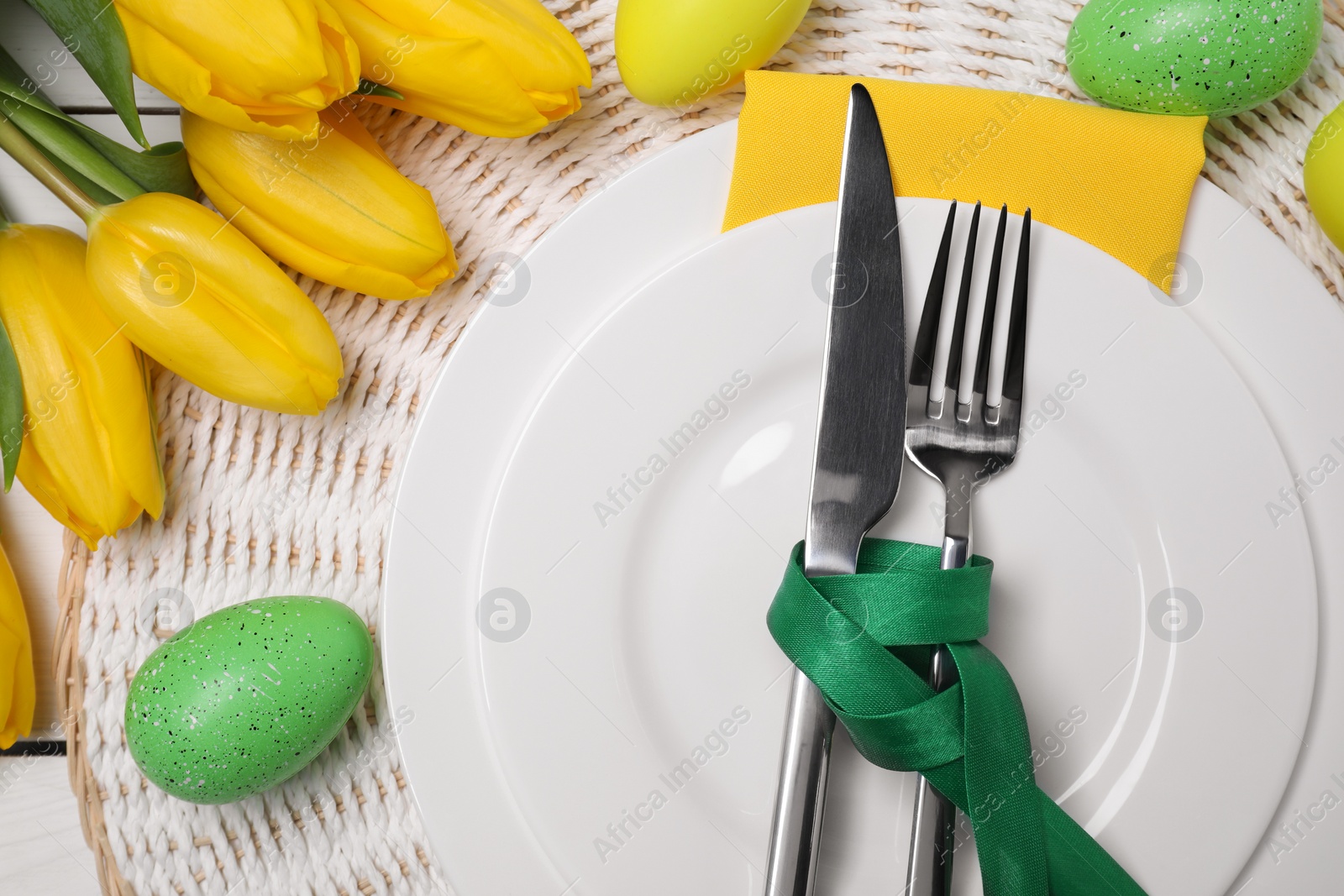 Photo of Festive table setting with painted eggs and tulips, flat lay. Easter celebration