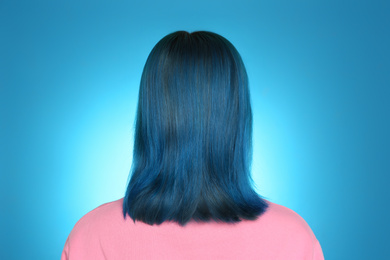 Woman with bright dyed hair on light blue background, back view