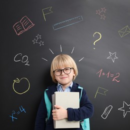 School boy holding notebooks near blackboard with chalk drawings and inscriptions