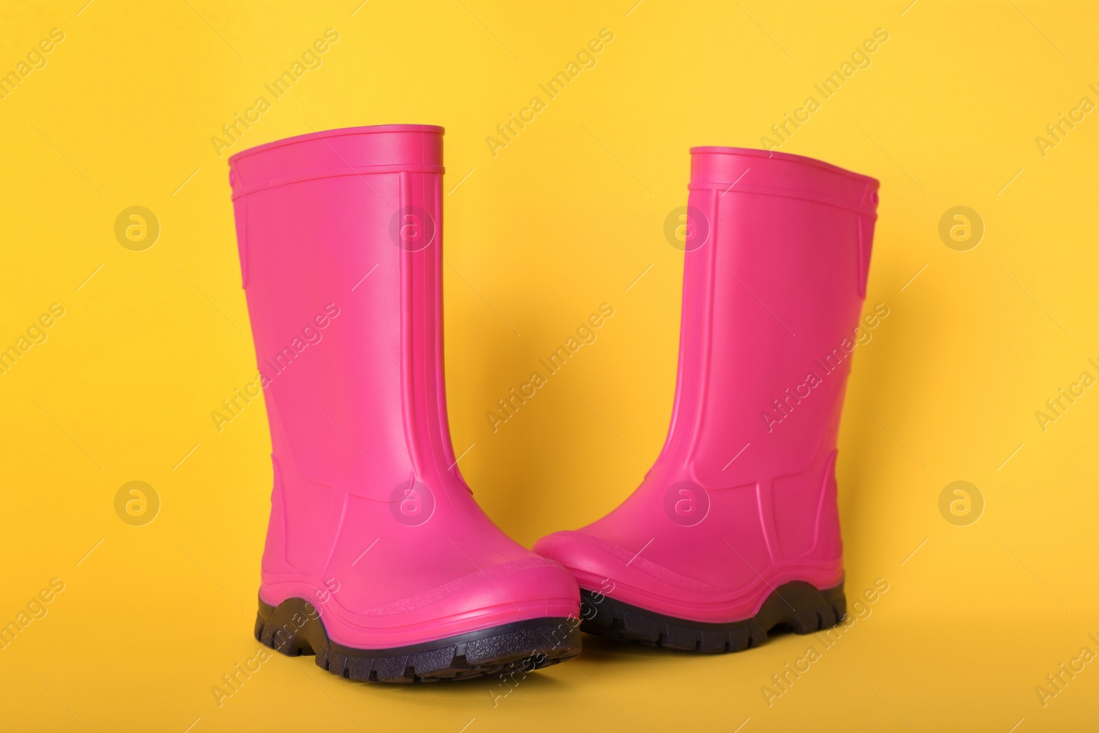 Photo of Pair of bright pink rubber boots on pale orange background