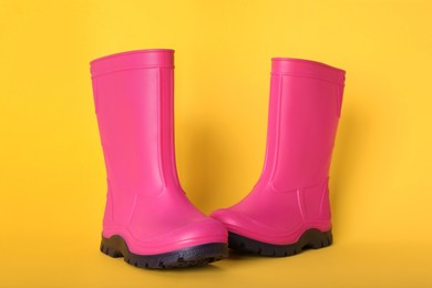 Photo of Pair of bright pink rubber boots on pale orange background