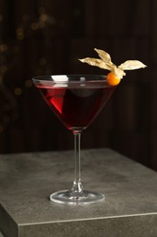Photo of Refreshing cocktail decorated with physalis fruit on grey table against blurred festive lights