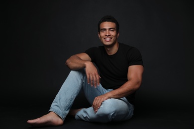 Handsome young African-American man sitting on black background