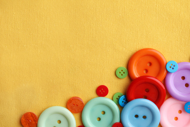 Many bright sewing buttons on yellow fabric, flat lay. Space for text