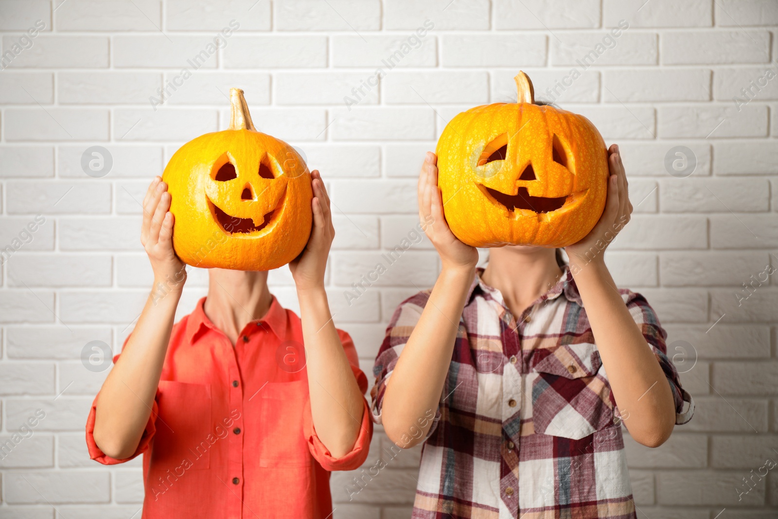 Photo of Women with pumpkin heads near white brick wall. Jack lantern - traditional Halloween decor
