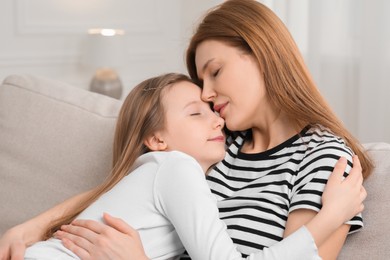 Mother hugging her cute daughter on sofa at home