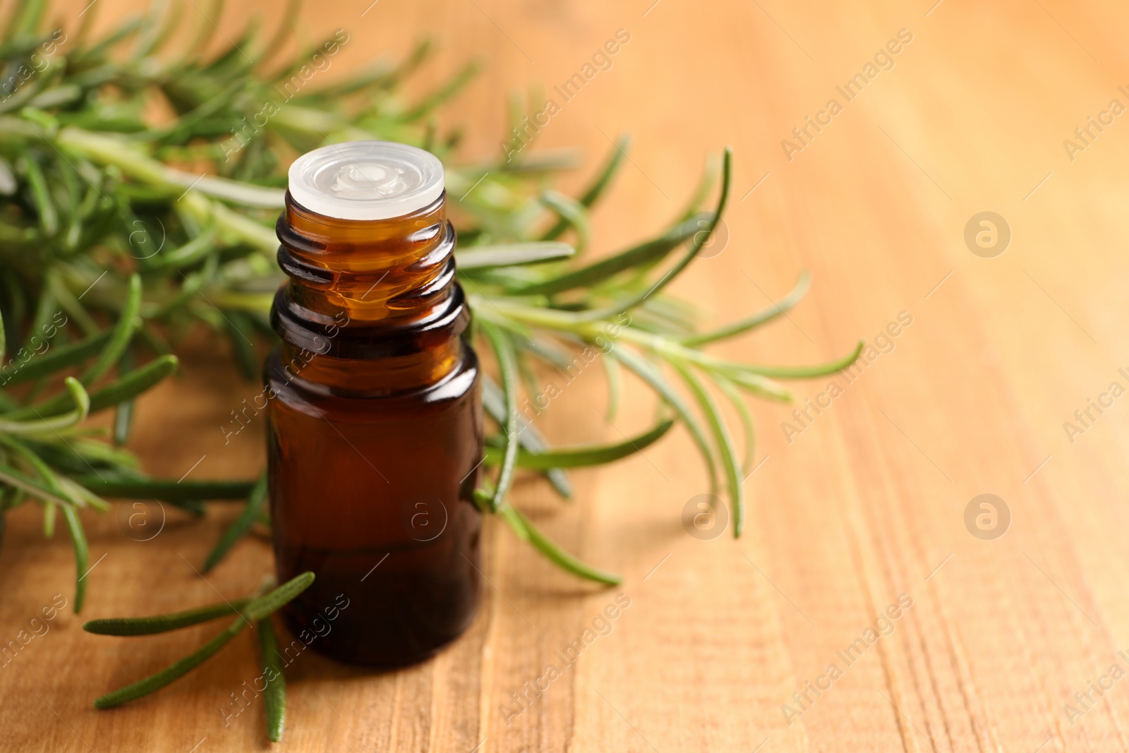 Photo of Bottle of rosemary oil and fresh twigs on wooden table, closeup. Space for text