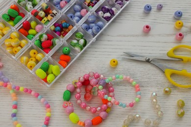 Photo of Beautiful handmade beaded jewelry and supplies on white wooden table, above view
