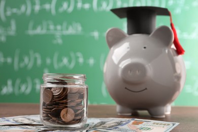 Photo of Scholarship concept. Glass jar with coins, piggy bank, graduation cap and dollar banknotes on wooden table