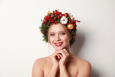 Beautiful young woman wearing Christmas wreath on white background