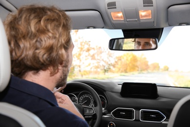 Photo of Young handsome man looking into interior mirror in car