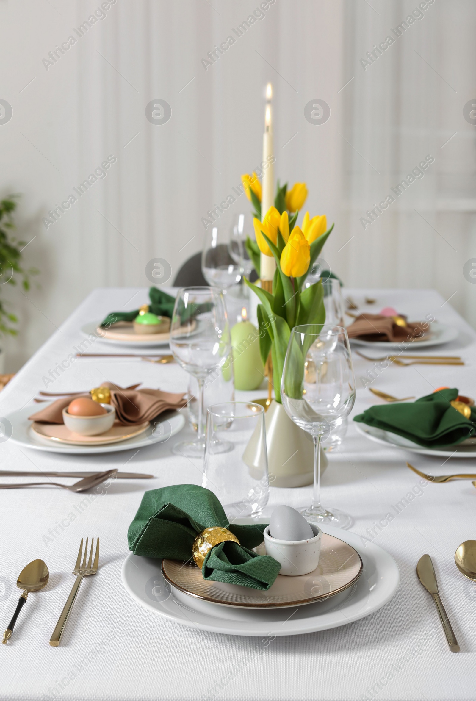 Photo of Festive Easter table setting with painted eggs, burning candles and yellow tulips indoors