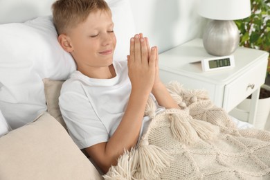 Photo of Boy with clasped hands praying in bed at home