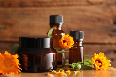 Different cosmetic products and beautiful calendula flowers on wooden table, closeup