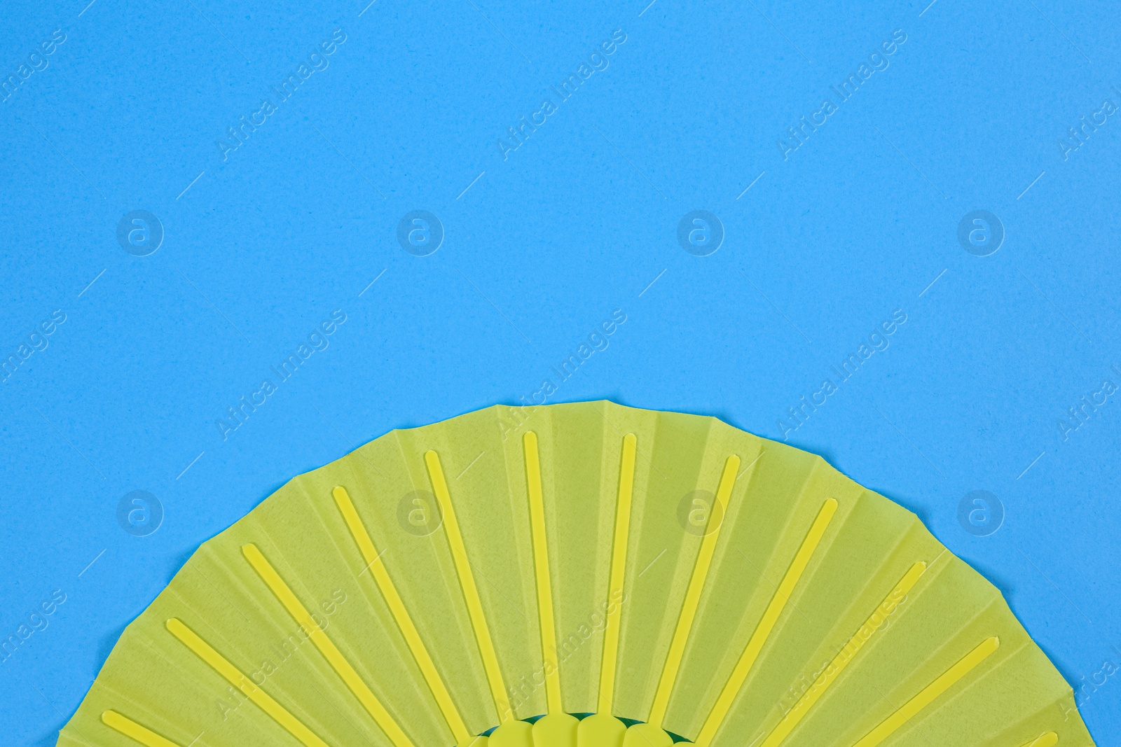 Photo of Yellow hand fan on light blue background, top view. Space for text