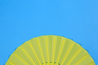 Yellow hand fan on light blue background, top view. Space for text