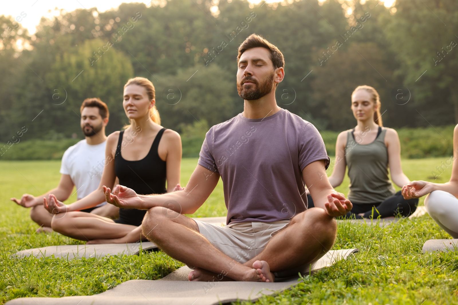 Photo of Group of people practicing yoga on mats outdoors. Lotus pose