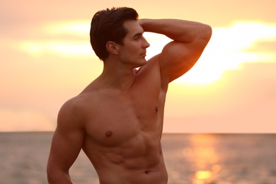 Handsome young man posing on beach near sea at sunset