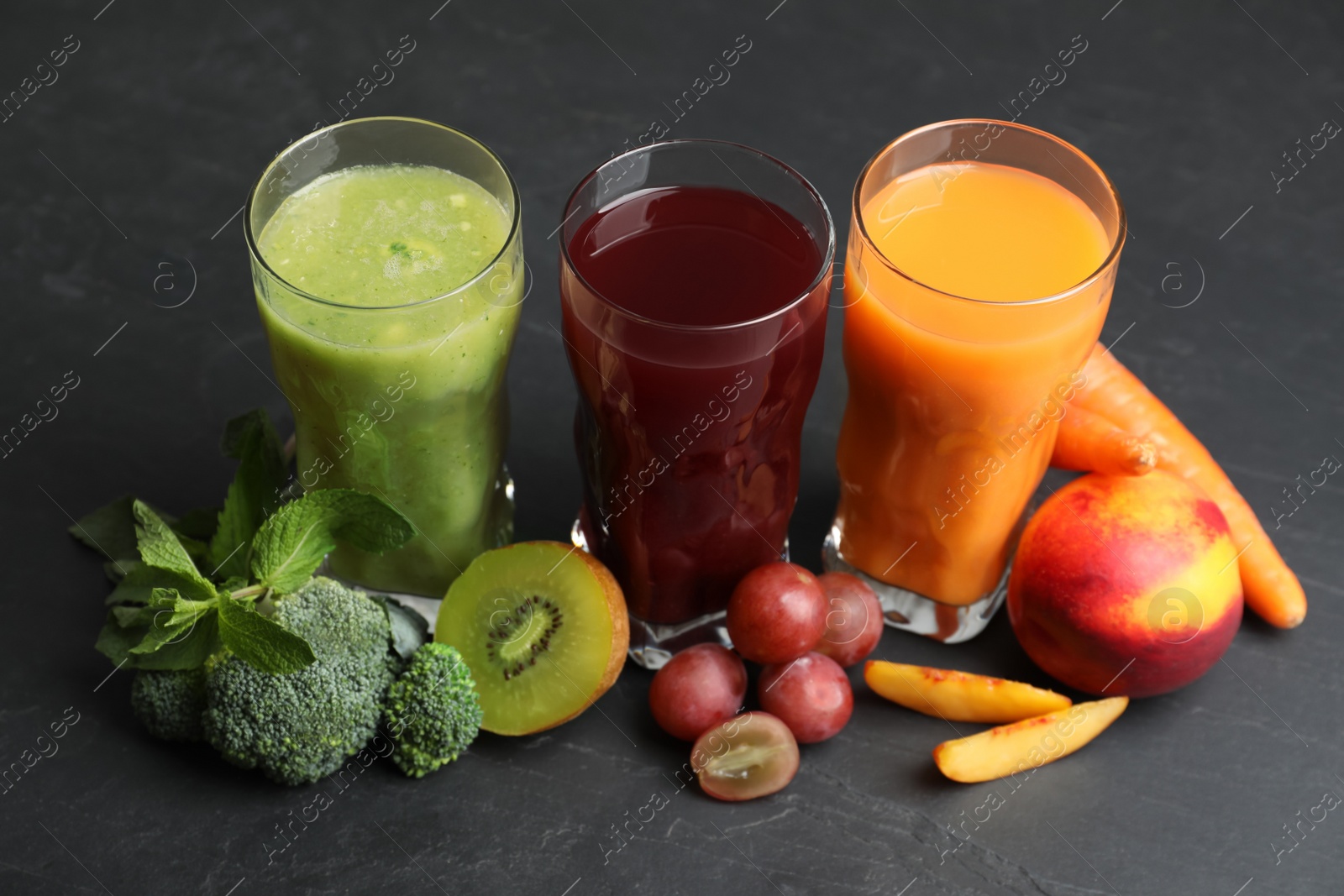 Photo of Delicious colorful juices in glasses and fresh ingredients on black table