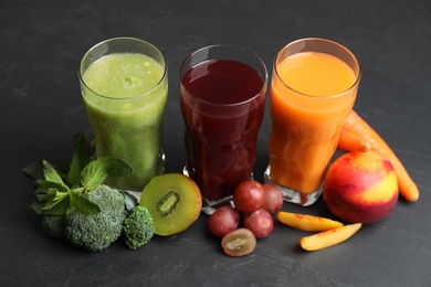 Photo of Delicious colorful juices in glasses and fresh ingredients on black table