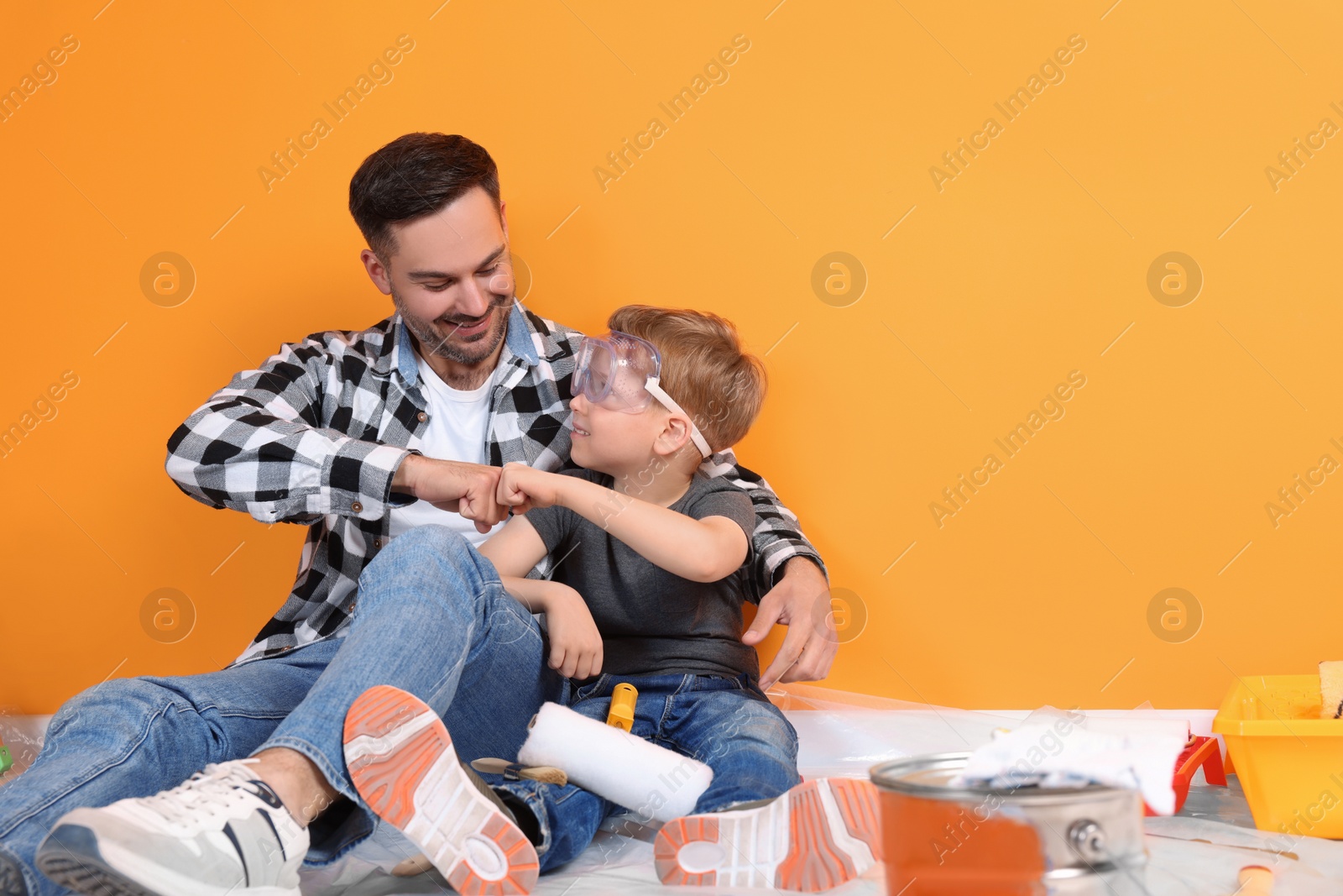 Photo of Father and son with repair tools near orange wall, space for text