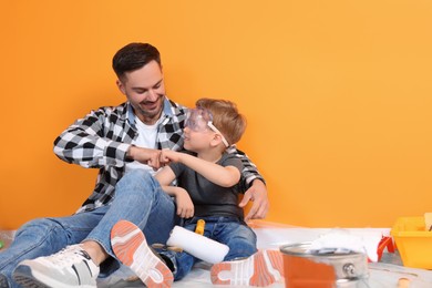 Father and son with repair tools near orange wall, space for text