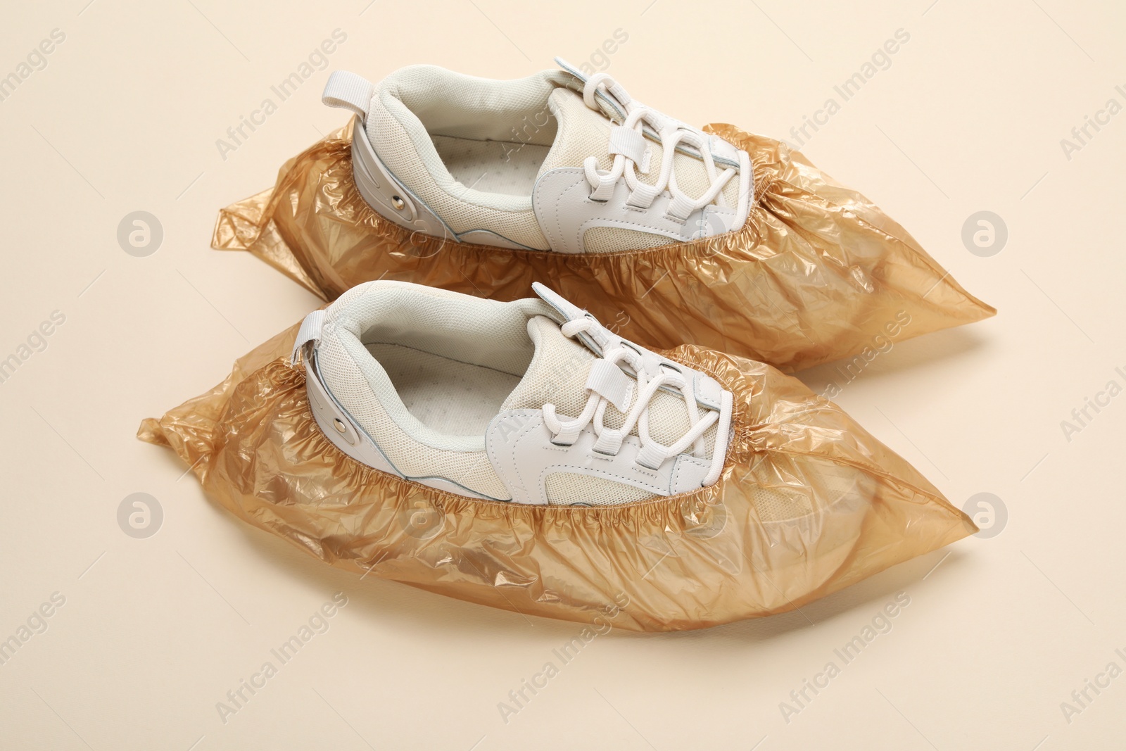 Photo of Sneakers in shoe covers on beige background, closeup