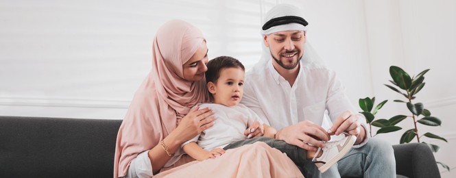 Happy Muslim family spending time together on sofa at home. Banner design 