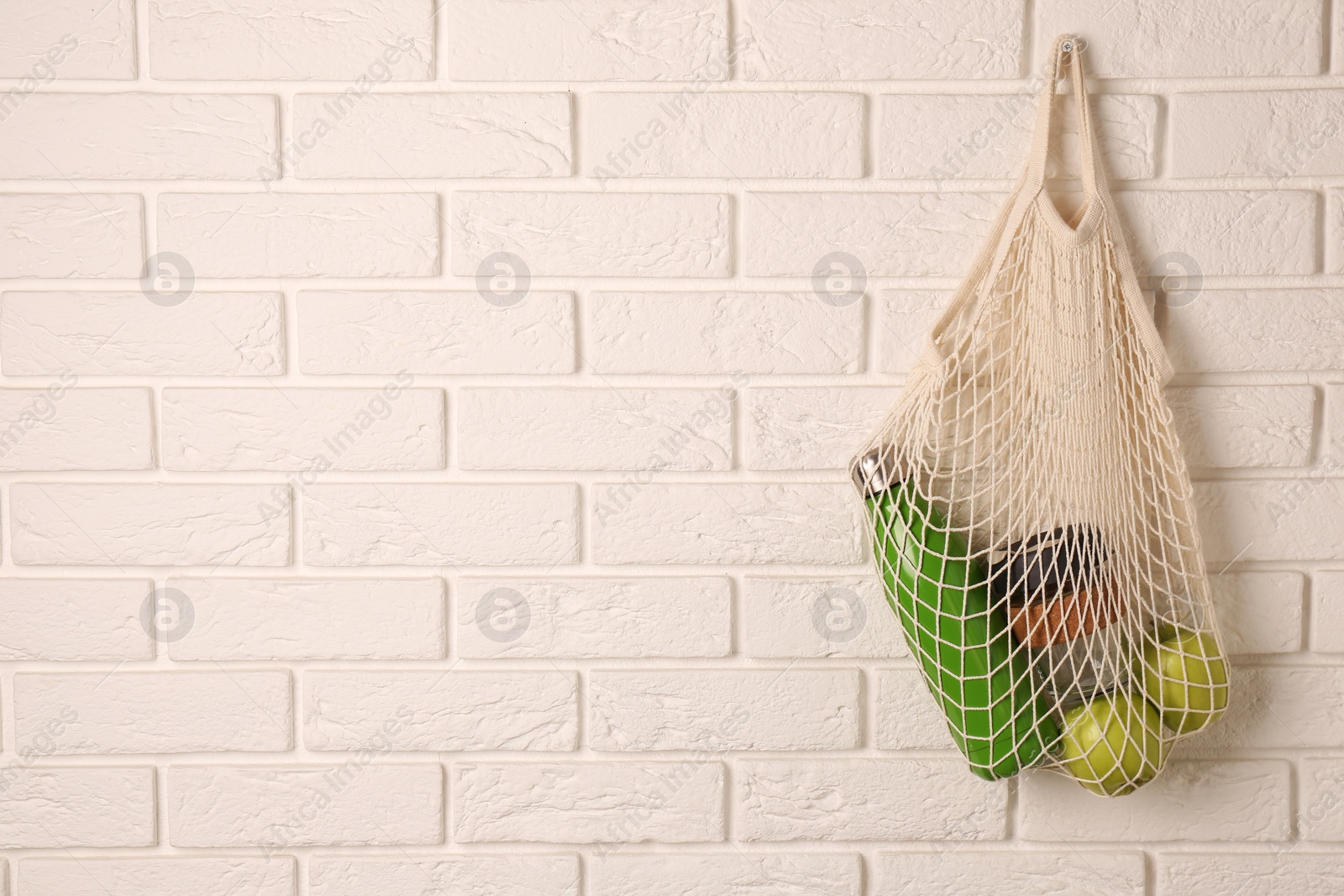 Photo of Net bag with different items hanging on brick wall, space for text. Conscious consumption