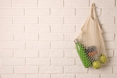 Photo of Net bag with different items hanging on brick wall, space for text. Conscious consumption