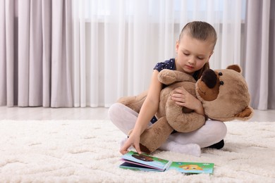 Photo of Cute little girl playing with teddy bear at home. Space for text