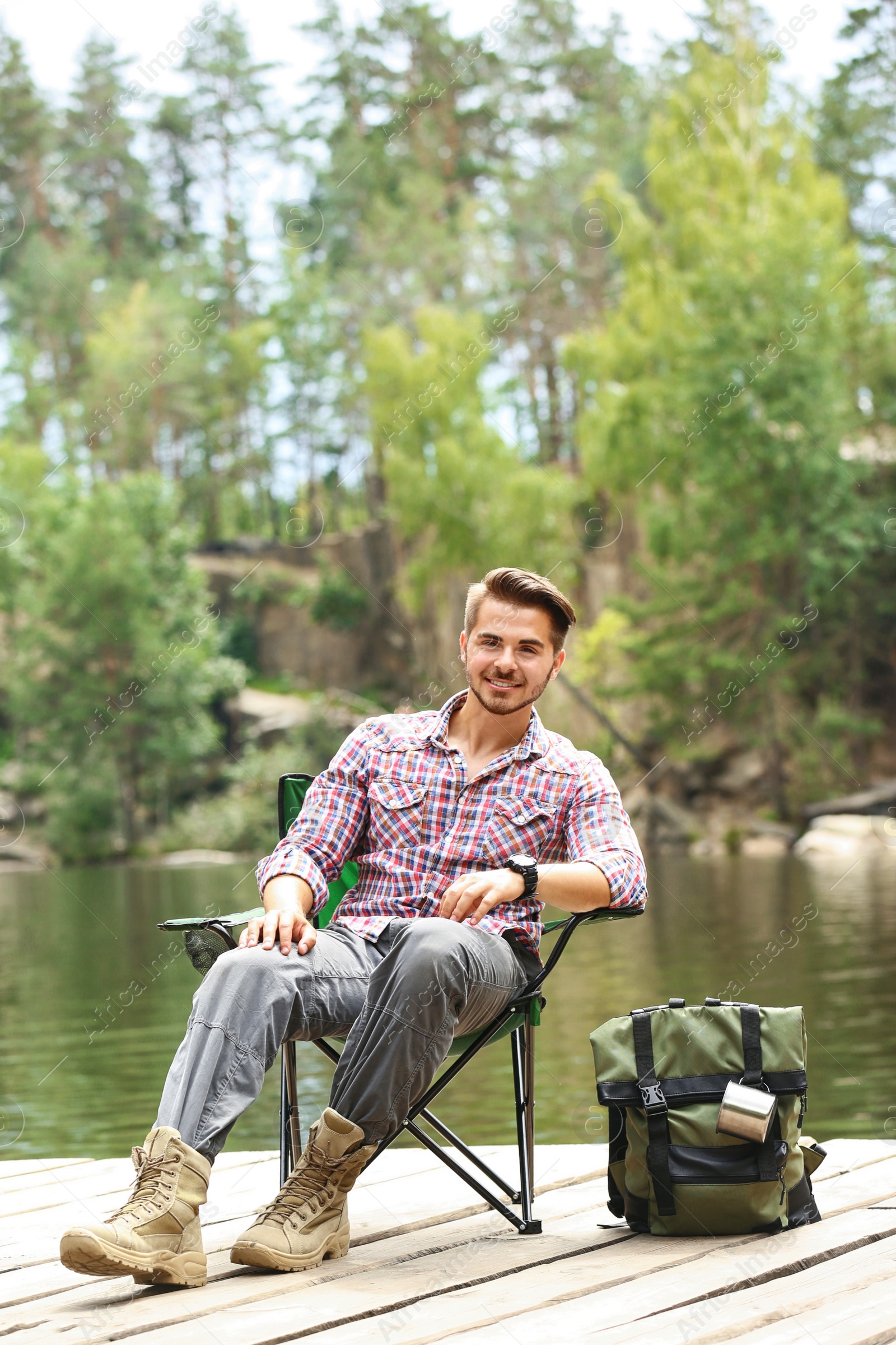 Photo of Young man resting on wooden pier near lake. Camping season