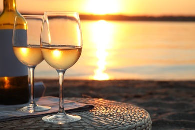 Photo of Bottle and glasses of delicious wine on riverside at sunset